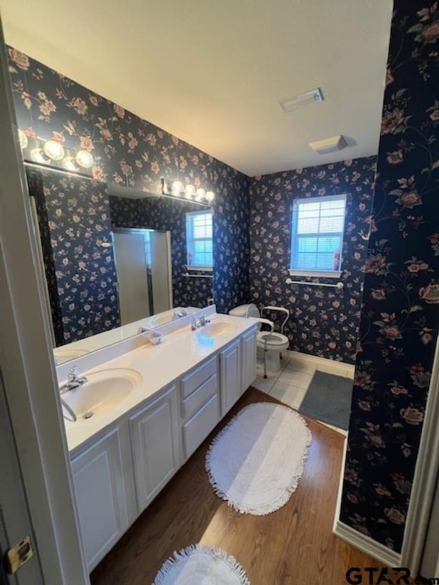 full bath featuring wallpapered walls, double vanity, wood finished floors, and a sink