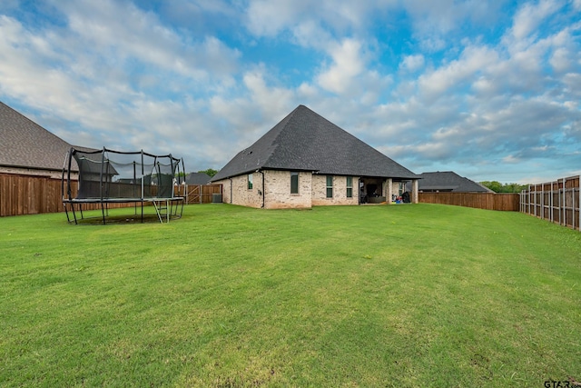 213 Serenity Dr, Bullard, TX 75757 - back of house featuring a trampoline, a shingled roof, brick siding, and a fenced backyard