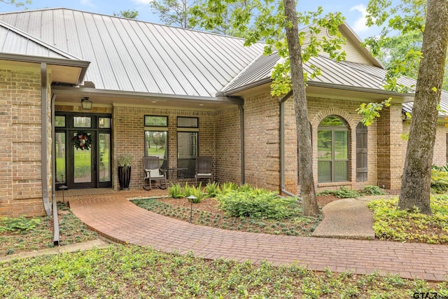view of exterior entry featuring brick siding, covered porch, a standing seam roof, and metal roof