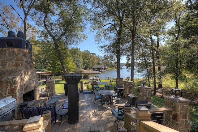 wooden terrace with grilling area, a water view, and an outdoor stone fireplace