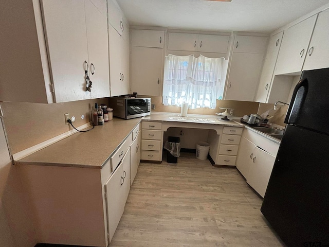 kitchen with white cabinets, light wood-type flooring, and black fridge