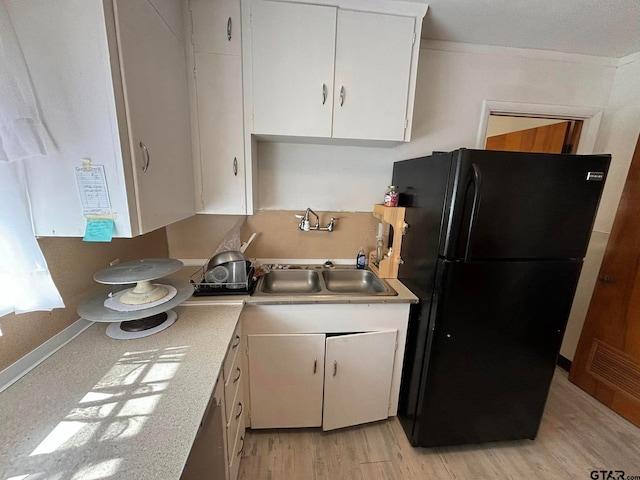 kitchen featuring black fridge, sink, crown molding, white cabinets, and light wood-type flooring