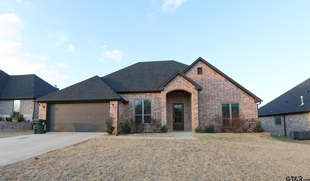 french country style house with a garage, a front yard, and central AC unit