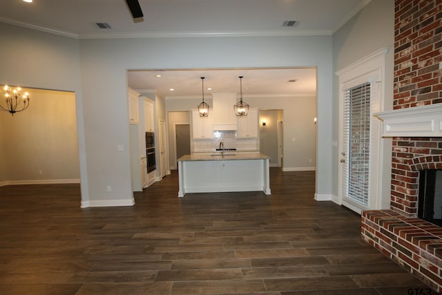 kitchen featuring an island with sink, a brick fireplace, pendant lighting, and light stone counters