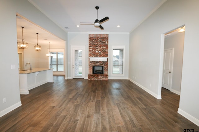 unfurnished living room with ceiling fan with notable chandelier, a fireplace, sink, dark hardwood / wood-style flooring, and ornamental molding