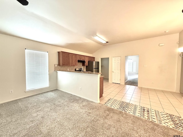 kitchen featuring brown cabinets, light tile patterned floors, light countertops, freestanding refrigerator, and a peninsula