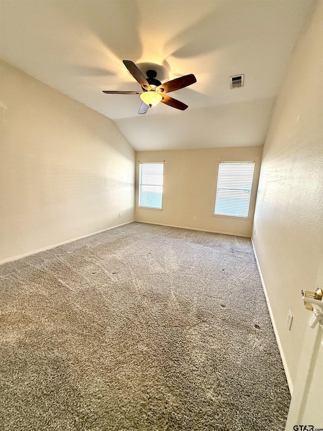 carpeted spare room with baseboards, visible vents, vaulted ceiling, and a ceiling fan