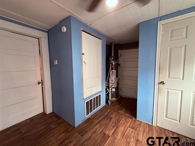 interior space with dark wood-type flooring, visible vents, and gas water heater