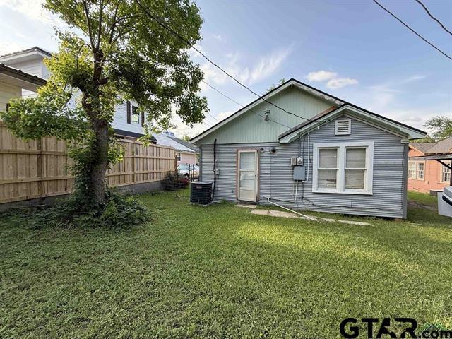 rear view of house featuring a lawn, central AC, and fence