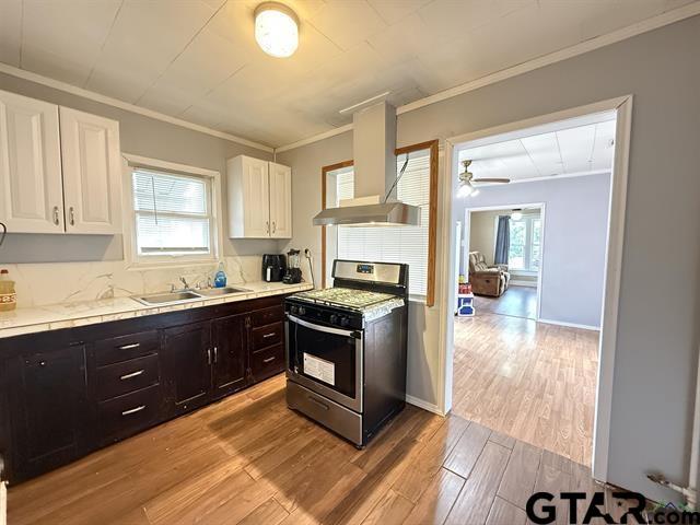 kitchen with gas stove, a sink, crown molding, wall chimney exhaust hood, and white cabinets