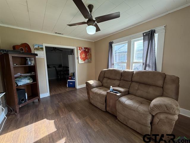 living area with dark wood-style flooring, ornamental molding, a ceiling fan, and visible vents