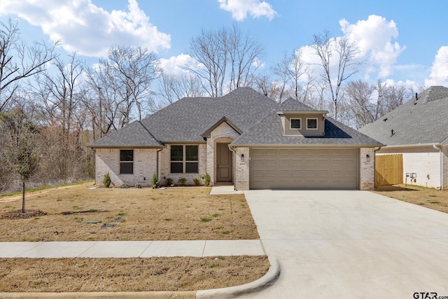 view of front of home featuring roof with shingles, brick siding, a garage, driveway, and a front lawn