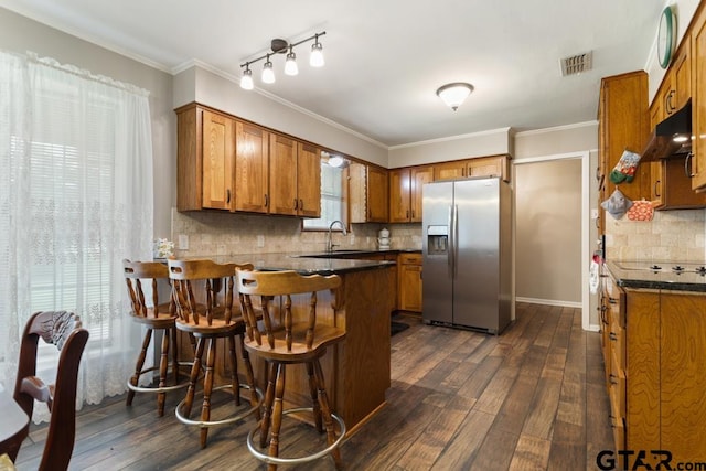 10516 Debbie Ln, Flint, TX 75762 - kitchen with stainless steel fridge with ice dispenser, brown cabinetry, dark countertops, a peninsula, and ornamental molding