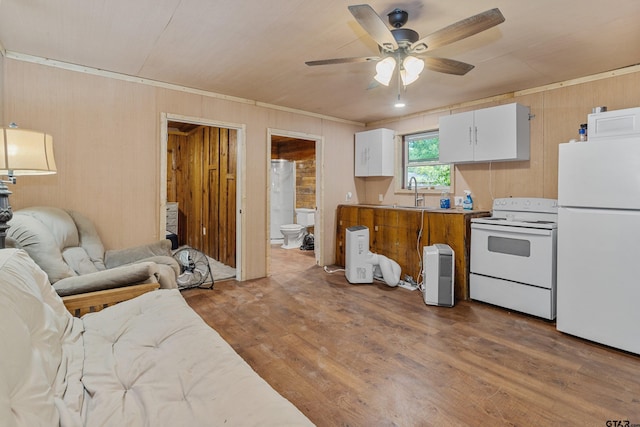 kitchen featuring open floor plan, white cabinetry, a sink, wood finished floors, and white appliances