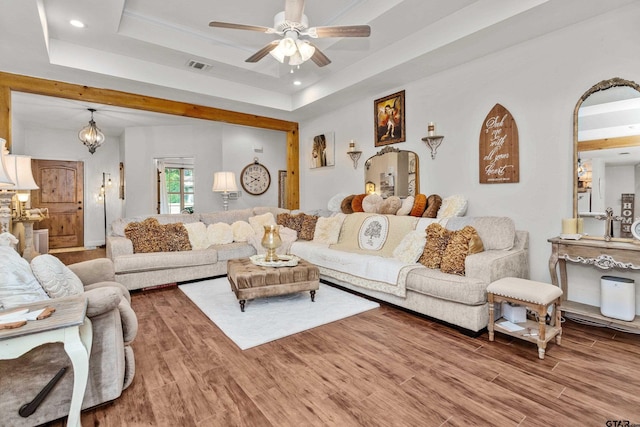 living room featuring ceiling fan with notable chandelier, wood finished floors, a raised ceiling, and visible vents