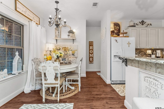 dining area with dark wood-style floors, baseboards, visible vents, and an inviting chandelier