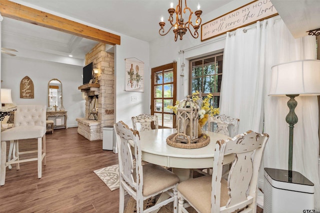 dining area with an inviting chandelier, wood finished floors, and a stone fireplace