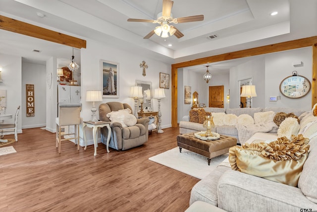 living room featuring baseboards, visible vents, a ceiling fan, a tray ceiling, and light wood-type flooring