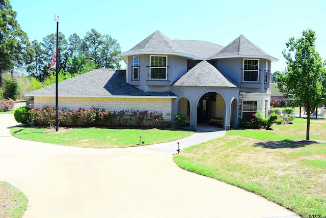 french country home with roof with shingles, stucco siding, a front lawn, and stone siding
