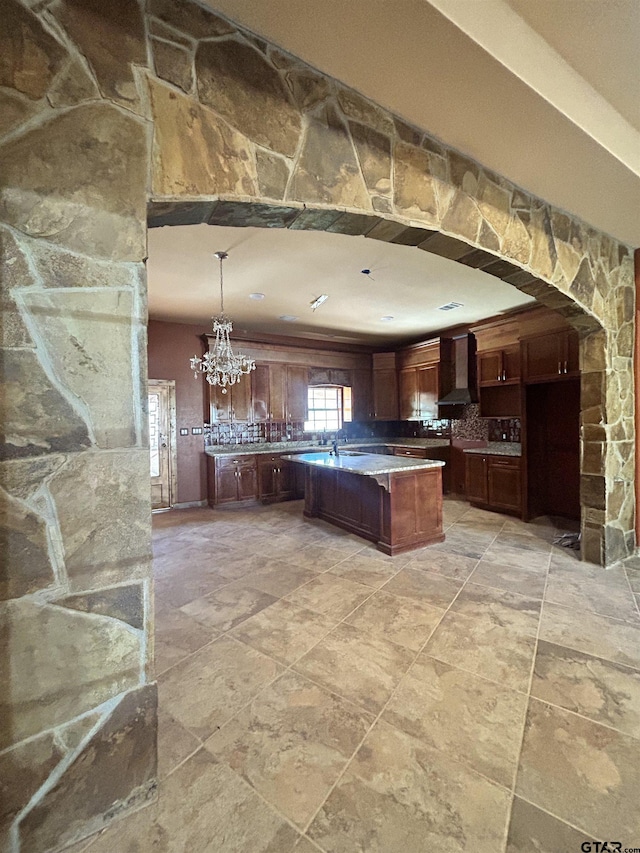 kitchen featuring pendant lighting, wall chimney exhaust hood, a center island, and a notable chandelier