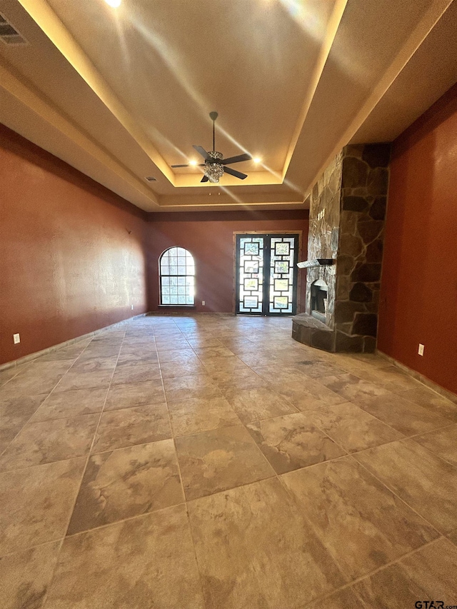 unfurnished living room with french doors, a stone fireplace, ceiling fan, and a tray ceiling