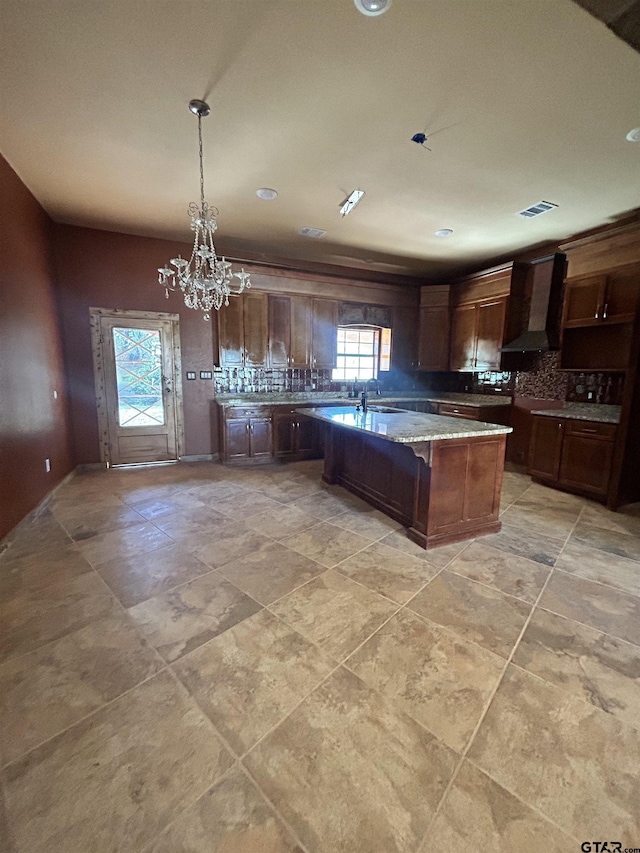 kitchen featuring pendant lighting, decorative backsplash, dark brown cabinets, and wall chimney range hood