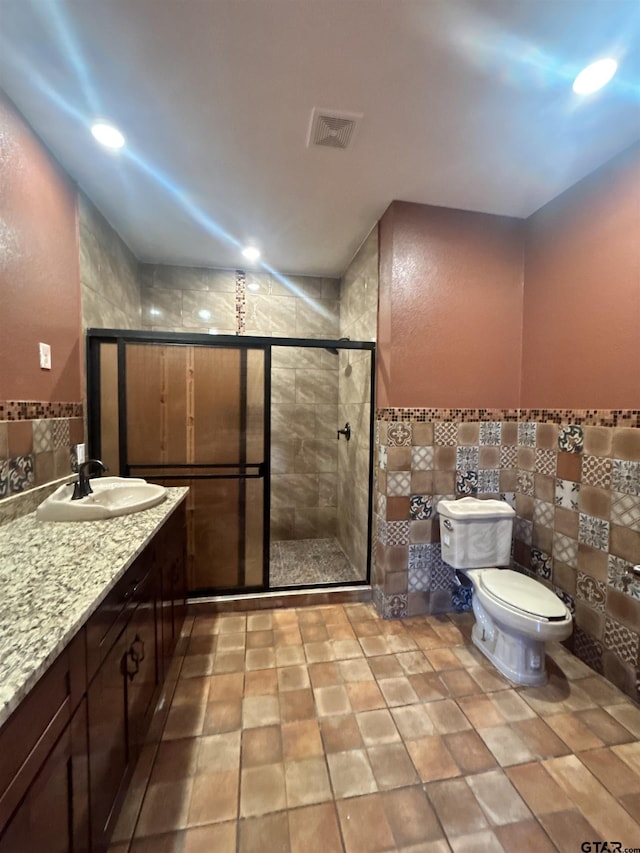 bathroom featuring toilet, tile walls, vanity, and a shower with shower door