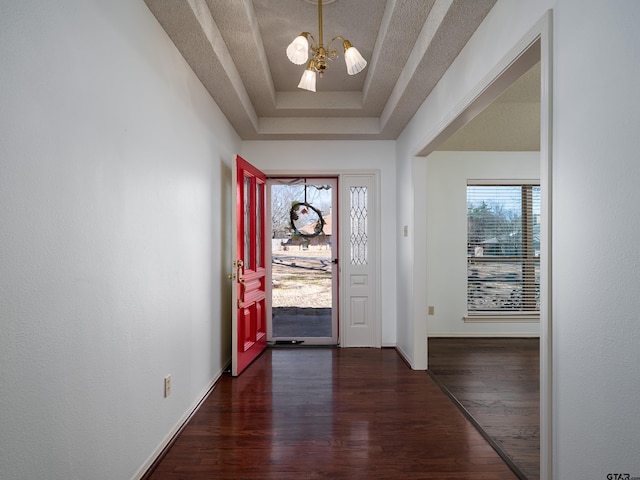 entryway with baseboards, dark wood finished floors, a tray ceiling, a textured ceiling, and a notable chandelier