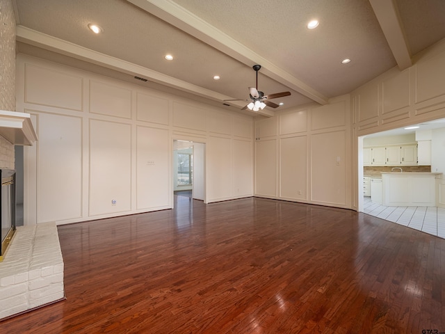 unfurnished living room with a decorative wall, a fireplace, wood finished floors, a ceiling fan, and beamed ceiling