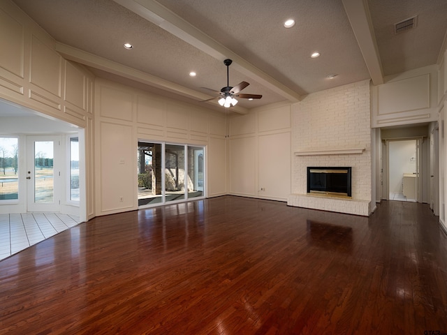 unfurnished living room featuring visible vents, a decorative wall, beamed ceiling, and wood finished floors