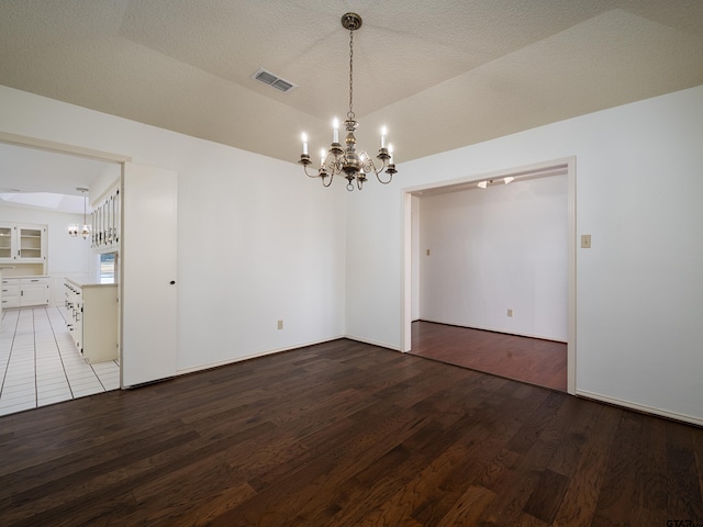 empty room featuring a textured ceiling, wood finished floors, visible vents, vaulted ceiling, and an inviting chandelier