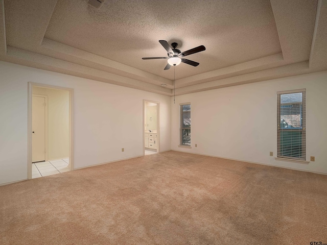 empty room with a textured ceiling, light tile patterned floors, light carpet, a ceiling fan, and a tray ceiling