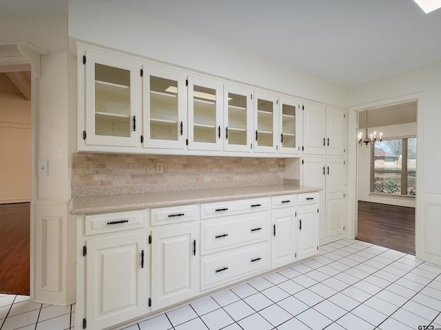 kitchen with glass insert cabinets, an inviting chandelier, light countertops, white cabinetry, and light tile patterned flooring