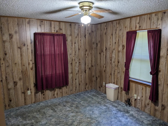 unfurnished bedroom with ceiling fan, a textured ceiling, wooden walls, and carpet