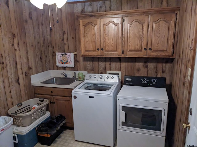 laundry area featuring cabinets, wood walls, washer and clothes dryer, and sink