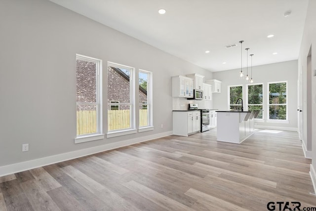 16330 Crossing Cir, Lindale, TX 75771 - kitchen featuring stainless steel appliances, dark countertops, white cabinets, a kitchen island with sink, and light wood-style flooring