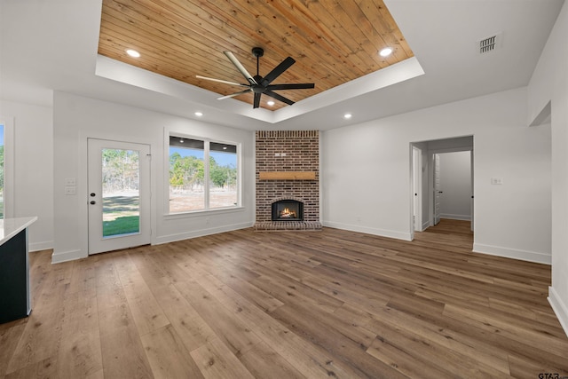 unfurnished living room with wood ceiling, a fireplace, a raised ceiling, light wood-type flooring, and ceiling fan