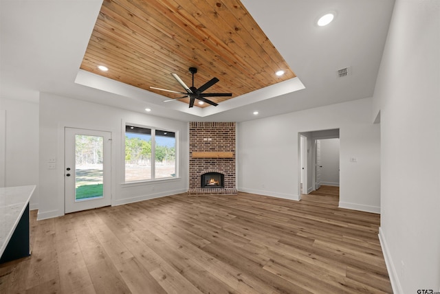 unfurnished living room featuring wood ceiling, a fireplace, light hardwood / wood-style floors, a raised ceiling, and ceiling fan