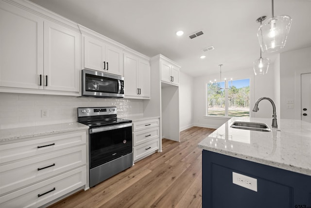 kitchen with appliances with stainless steel finishes, white cabinetry, sink, hanging light fixtures, and light hardwood / wood-style flooring