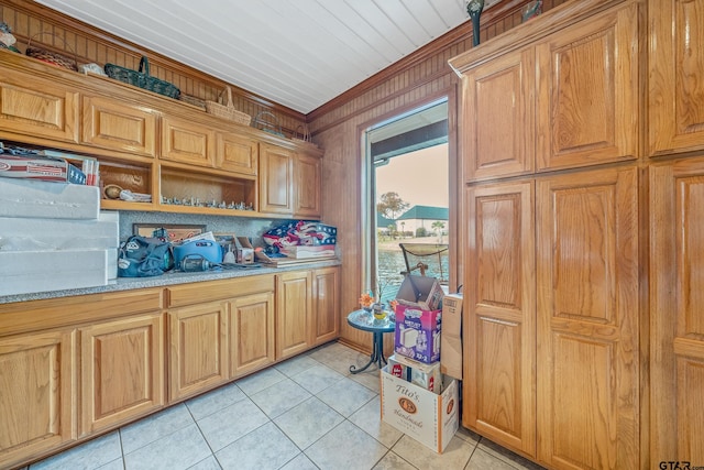 kitchen featuring wooden walls, light stone counters, ornamental molding, and light tile patterned flooring