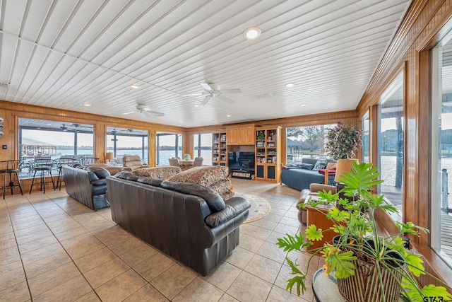 living room featuring wood walls, a water view, ceiling fan, light tile patterned floors, and wood ceiling