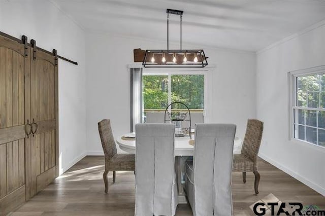 dining area featuring baseboards, a barn door, ornamental molding, and wood finished floors