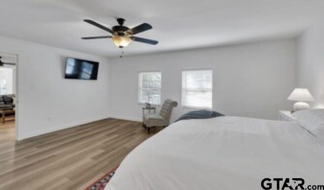 bedroom featuring a ceiling fan, baseboards, multiple windows, and wood finished floors