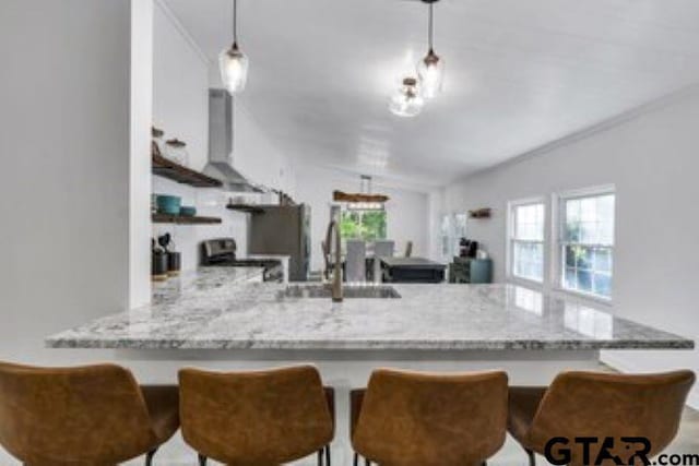 kitchen with wall chimney range hood, a sink, light stone counters, a peninsula, and stainless steel range oven