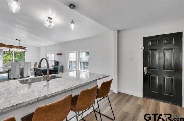 kitchen featuring light stone countertops, a breakfast bar, a sink, and light wood-style floors