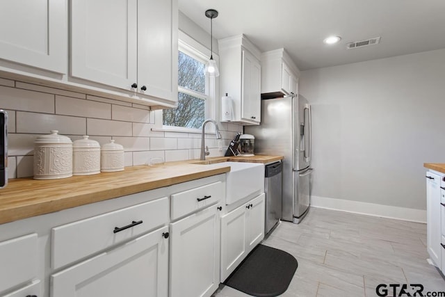 kitchen with hanging light fixtures, dishwasher, white cabinets, decorative backsplash, and wooden counters