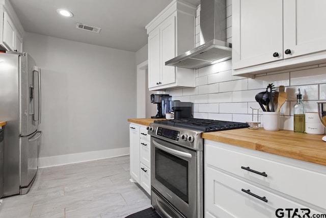 kitchen with appliances with stainless steel finishes, wall chimney range hood, white cabinets, and butcher block countertops