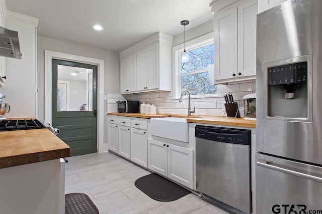 kitchen with white cabinets, stainless steel appliances, pendant lighting, and butcher block countertops