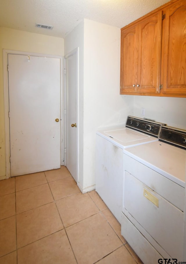 clothes washing area featuring cabinets, light tile patterned flooring, washer and dryer, and a textured ceiling