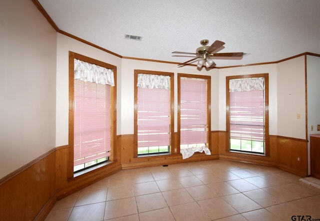 interior space featuring light tile patterned floors, crown molding, ceiling fan, a textured ceiling, and wood walls